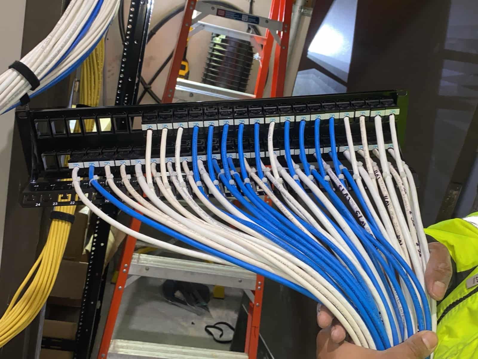 Technician holding a 48-port patch panel with blue and white Cat6 cables terminated in order