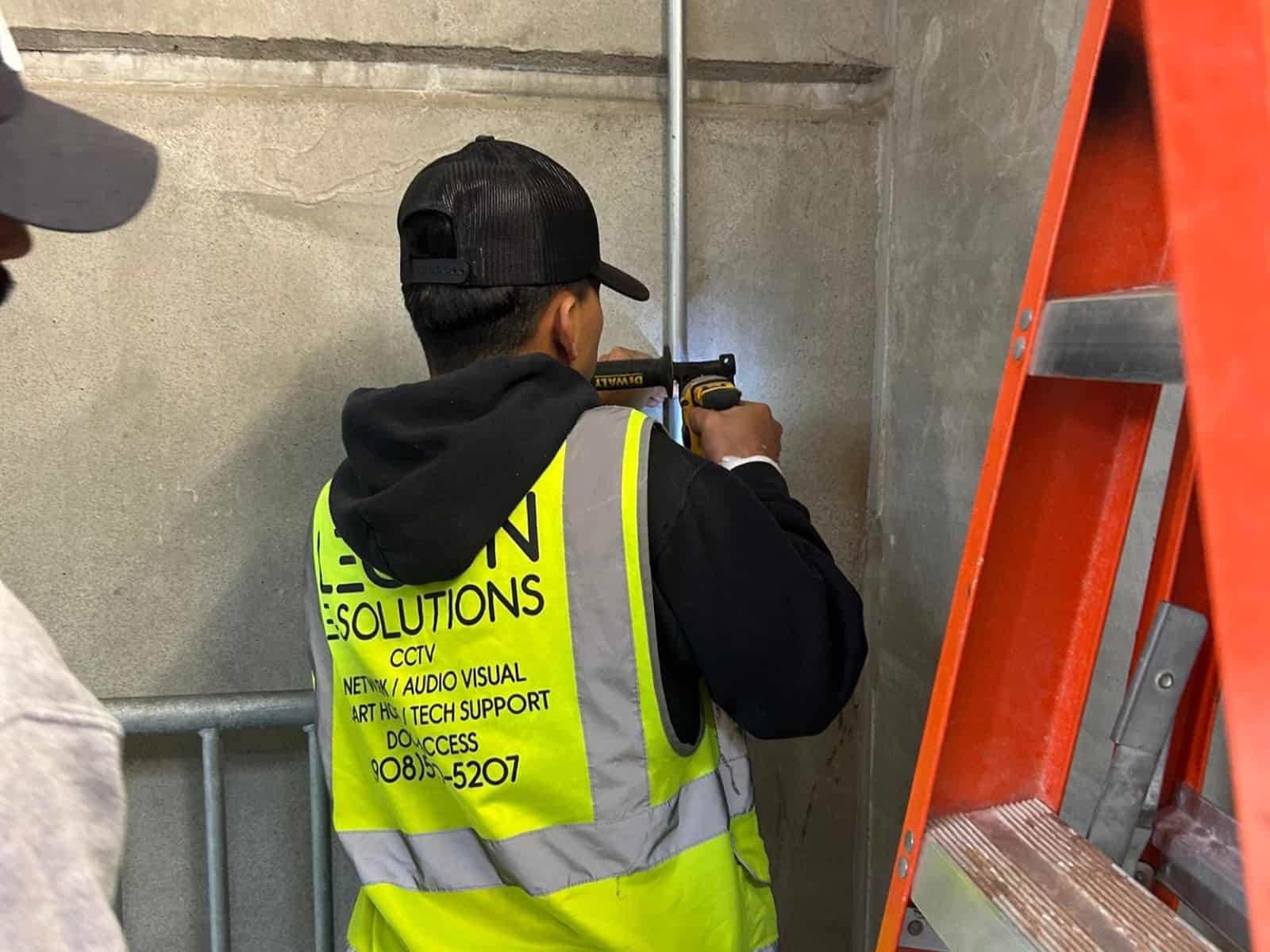 Legion E-Solutions technician drilling to mount conduit on a concrete stairwell wall