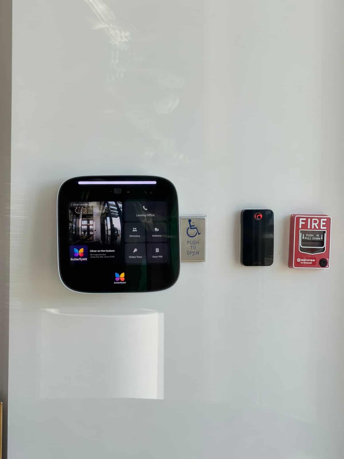 Video intercom touchscreen and card reader mounted beside a fire pull station in an apartment lobby