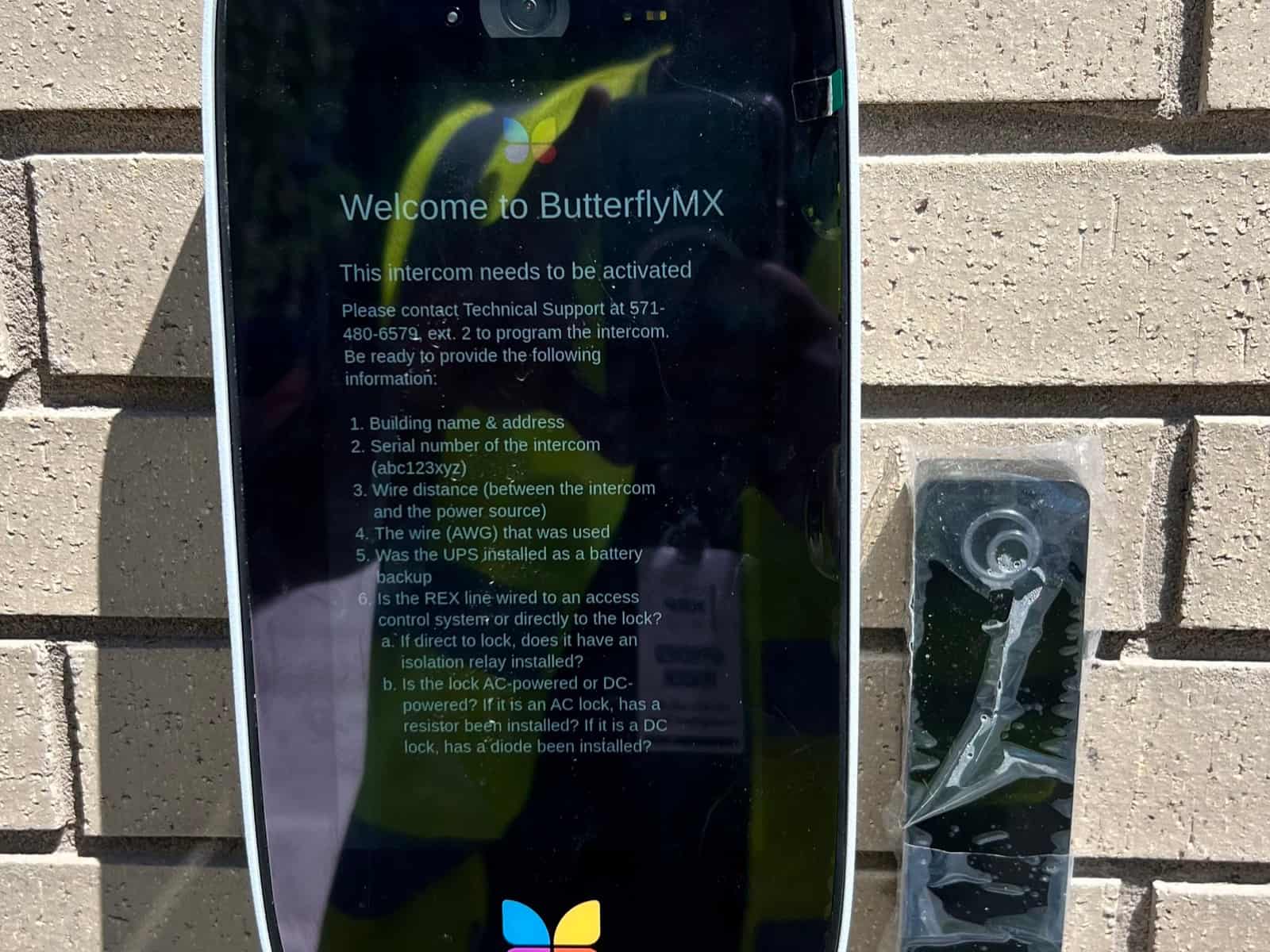 Newly mounted video intercom panel on a brick wall showing its activation screen, with a card reader still in packaging alongside