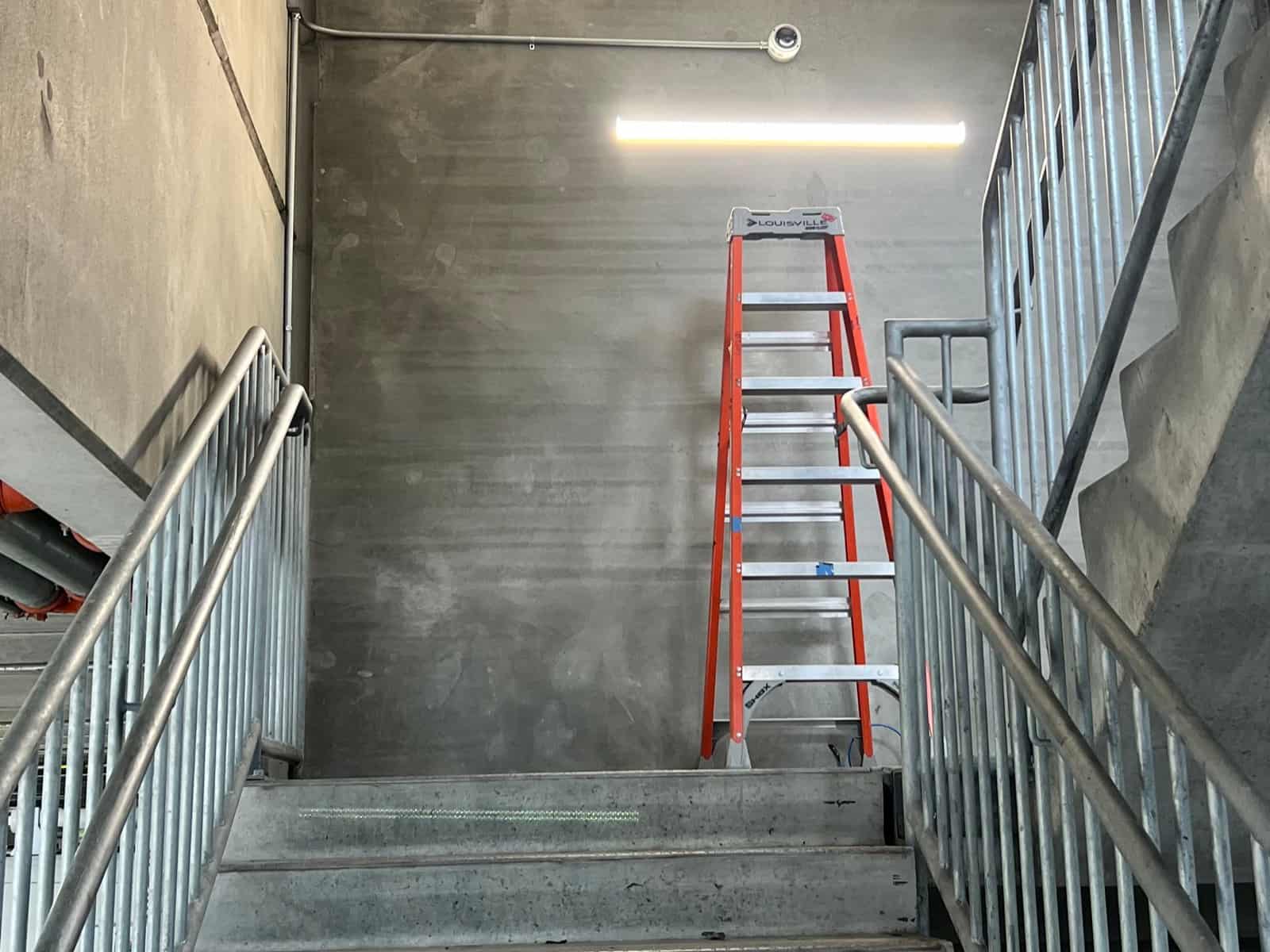 Camera on conduit above a concrete parking garage stairwell with a ladder set up below