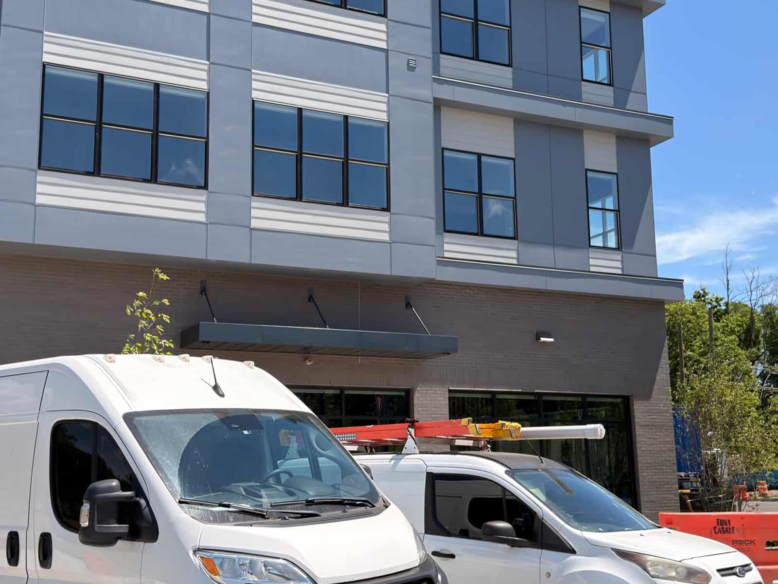 Two work vans parked outside a newly built mid-rise apartment building