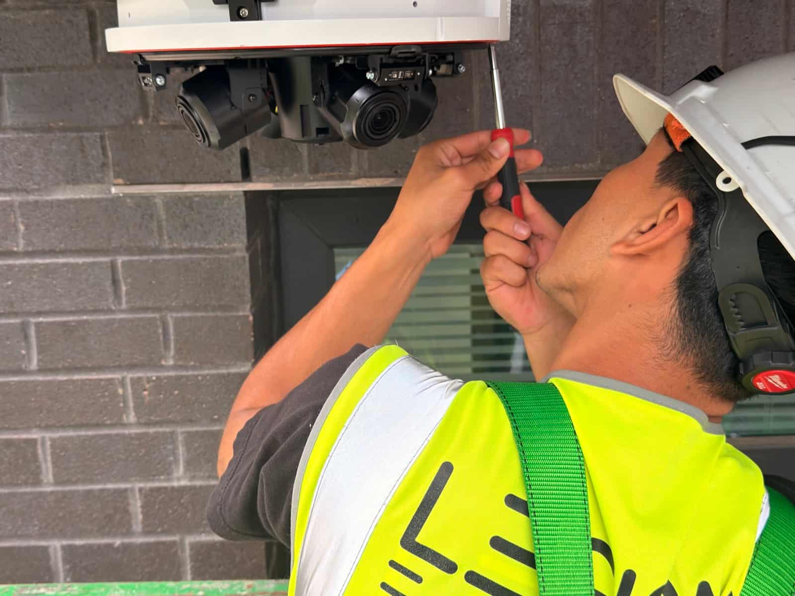Legion E-Solutions technician in a branded hi-vis vest and hard hat adjusting a multi-sensor camera mounted under a soffit