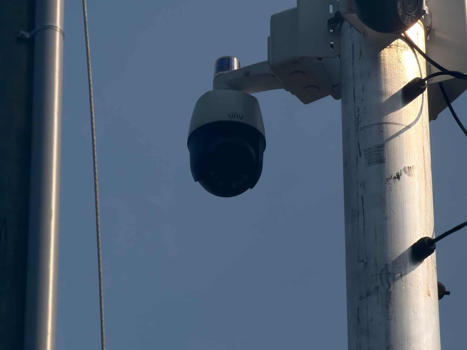 Two pole-mounted PTZ cameras with warning beacons against a clear sky