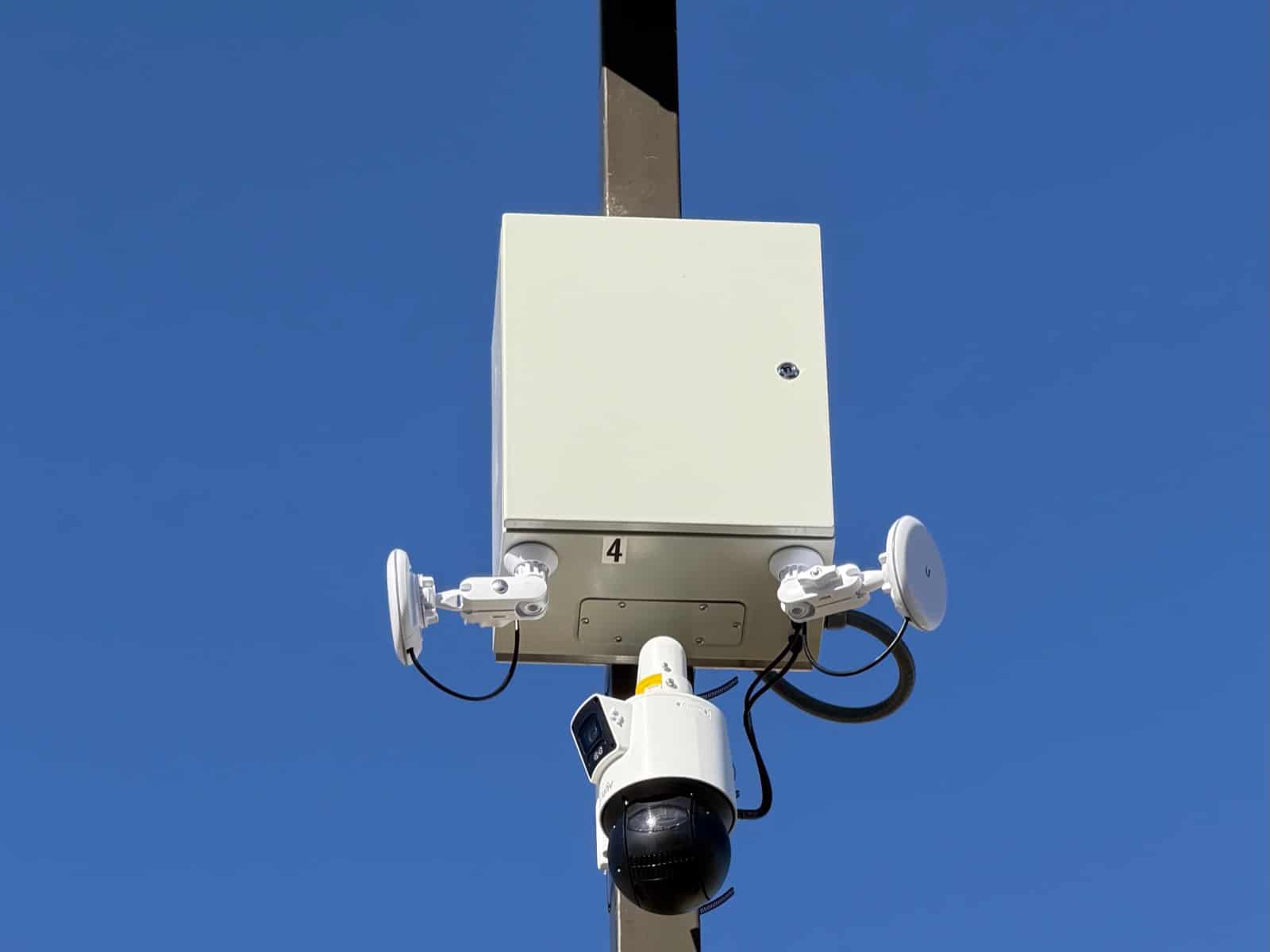 Light pole carrying a weatherproof equipment enclosure, two point-to-point wireless dishes and a PTZ camera