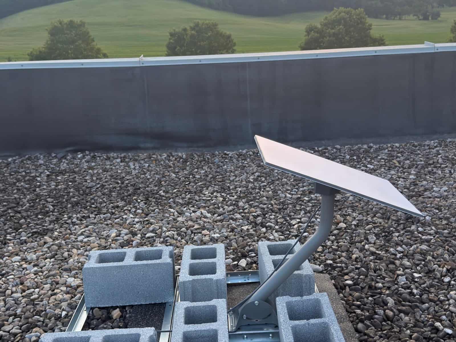 Satellite internet dish on a ballasted non-penetrating roof mount at sunrise