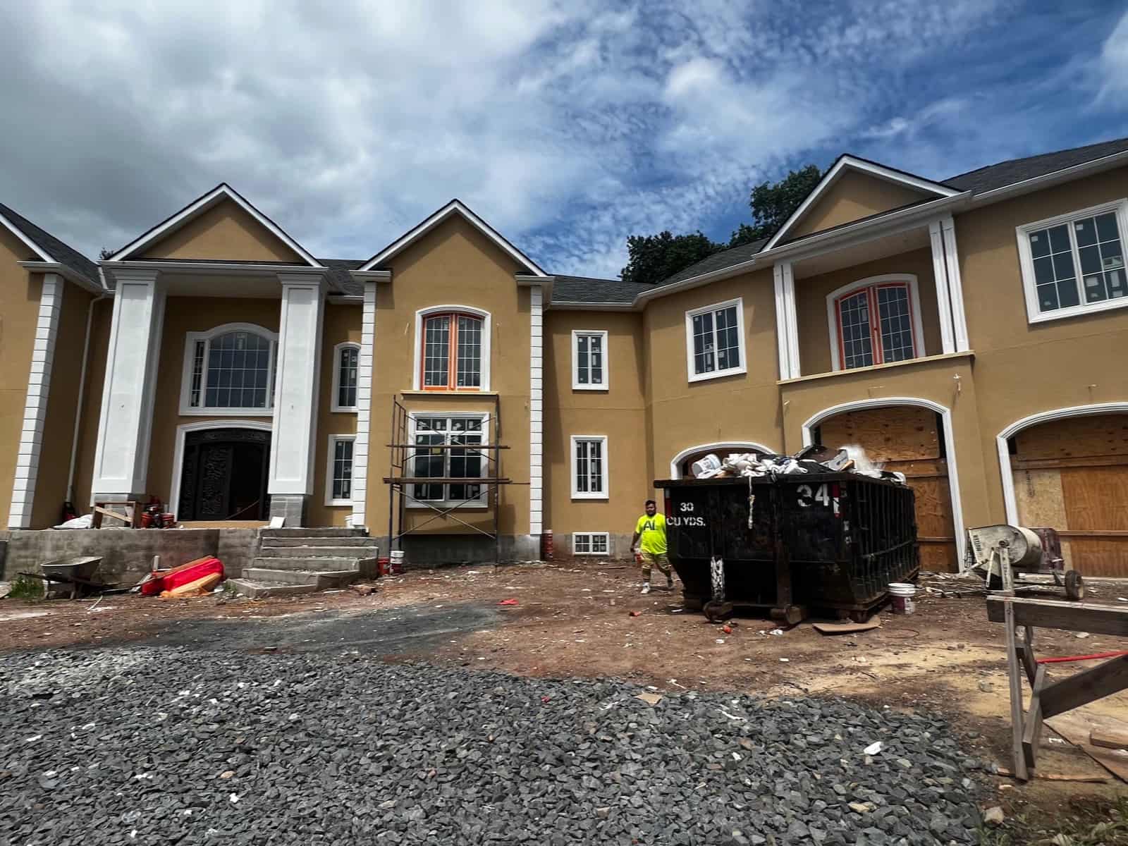 Large custom home under construction with scaffolding and a dumpster in the front yard